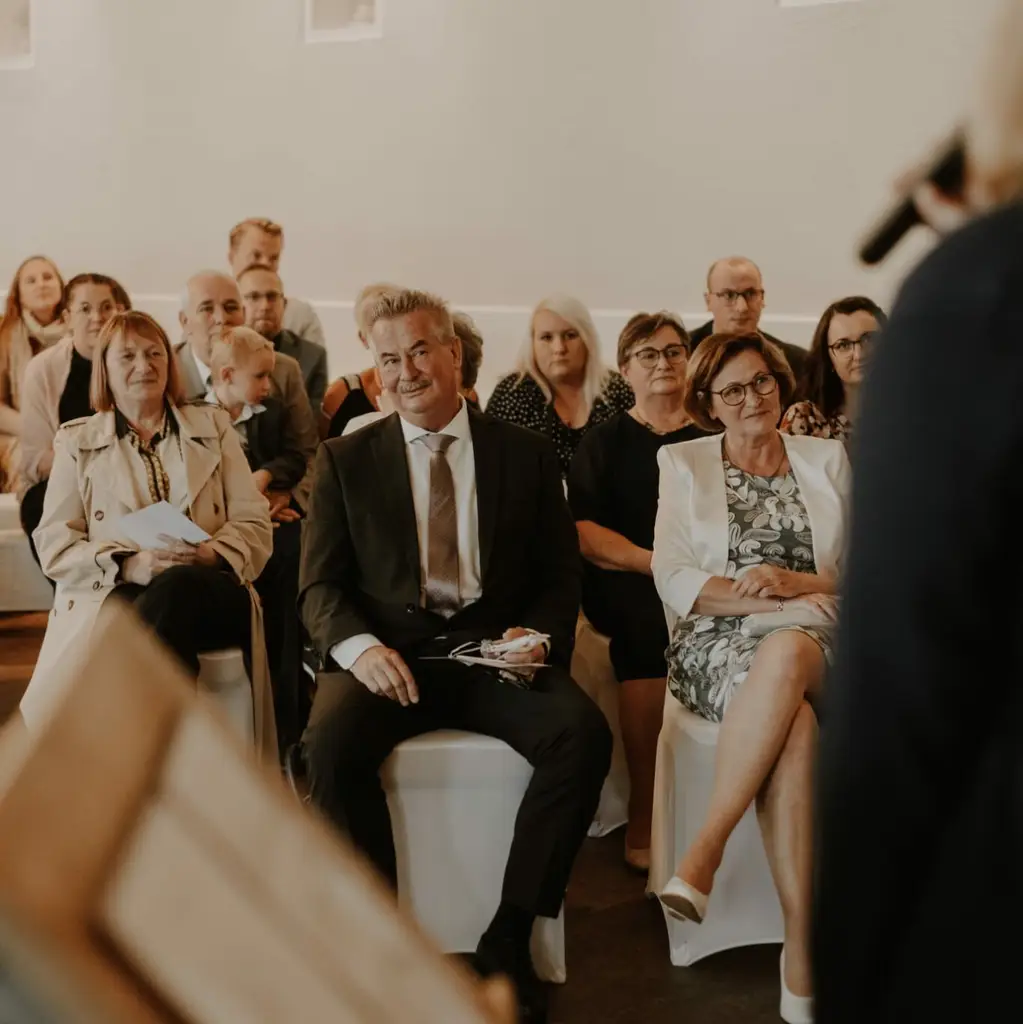 Hochzeitsgesellschaft, die im Festsaal der Freien Rednerin Christine Väätäjä lauscht und dabei lacht